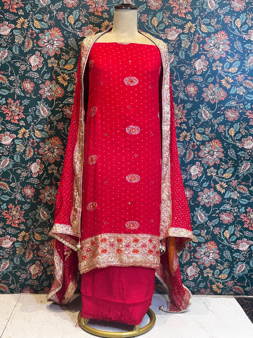 Red traditional outfit with gold embroidery on a mannequin against a floral wallpapered wall.