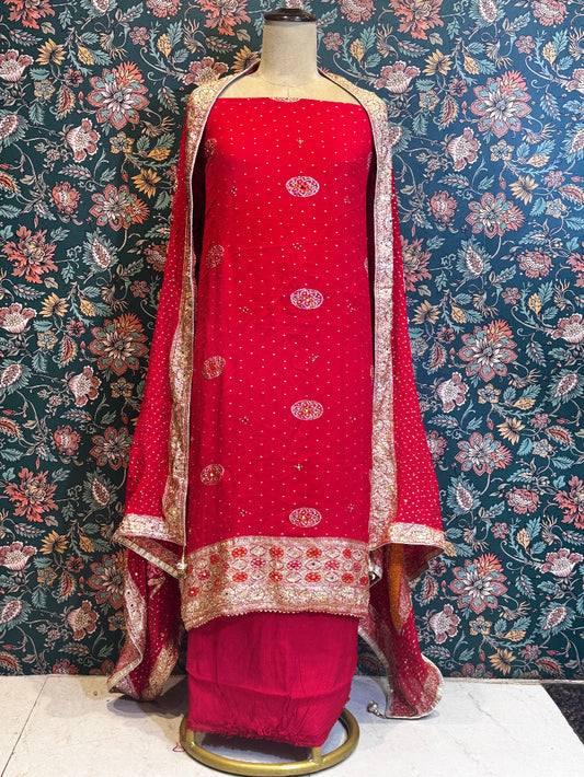 Red traditional outfit with gold embroidery on a mannequin against a floral wallpapered wall.