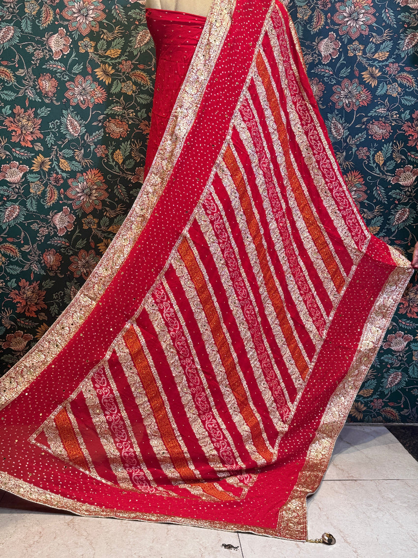 Red and gold patterned fabric draped over a surface with floral wallpaper in the background