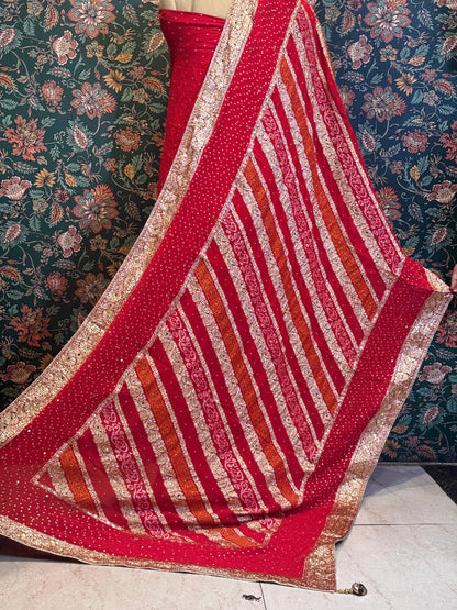 Red and gold patterned fabric draped over a surface with floral wallpaper in the background