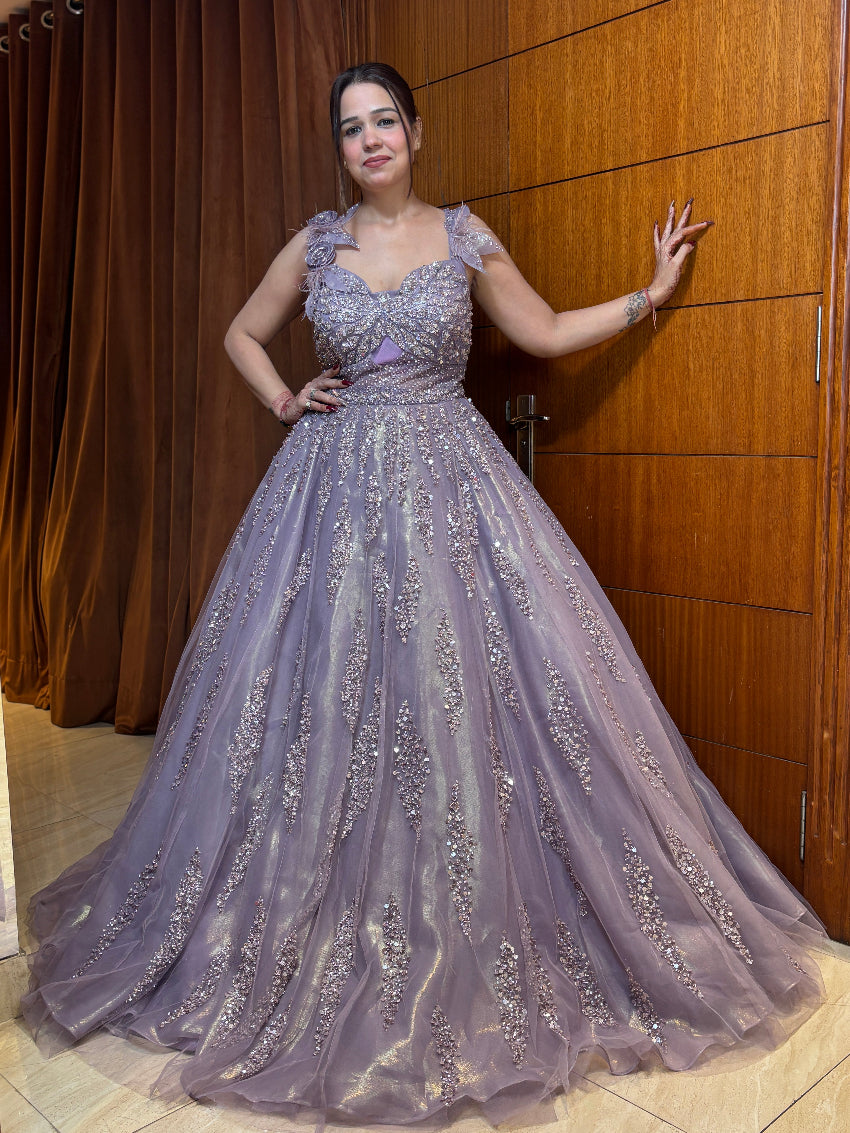 Woman in a purple evening gown standing against a wooden panel wall.
