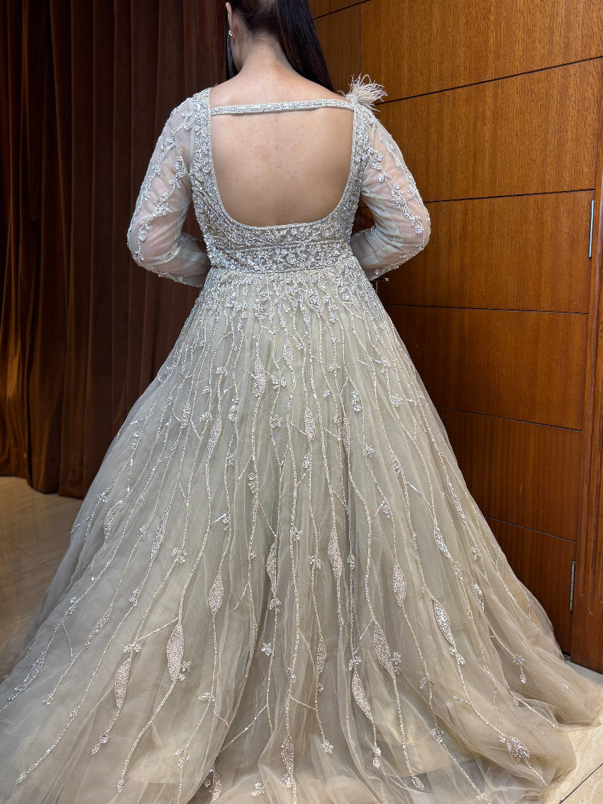 Elegant beige evening gown with intricate detailing in front of a wooden panel.