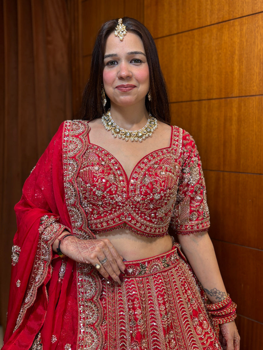 Woman in traditional red and gold embroidered outfit with jewelry against a wooden background