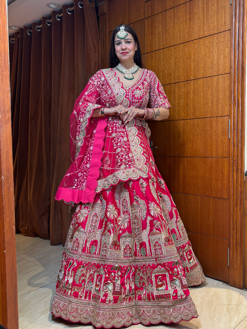 Woman in a traditional pink and red embroidered outfit standing indoors.