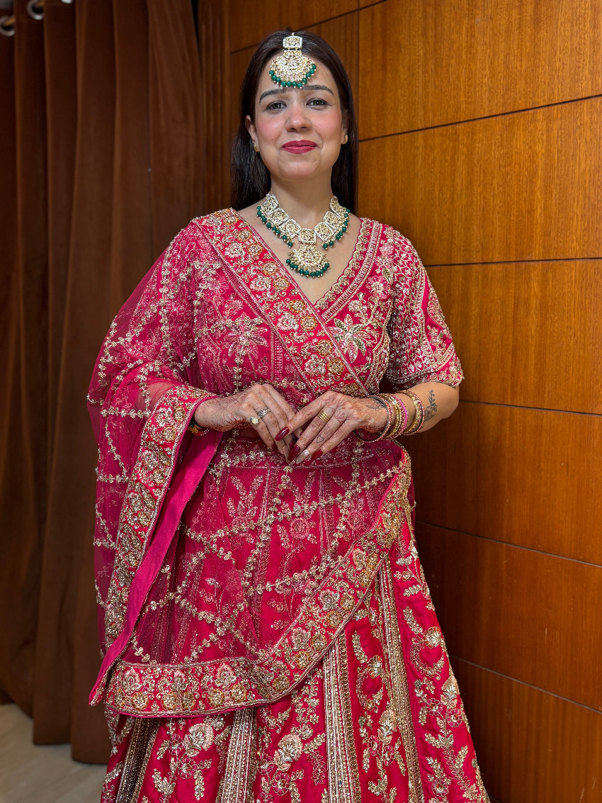 Woman in a traditional pink and gold embroidered outfit with jewelry against a wooden panel background