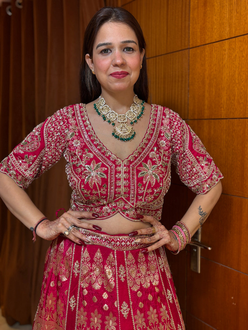 Woman wearing a traditional red and gold embroidered outfit with jewelry against a wooden background
