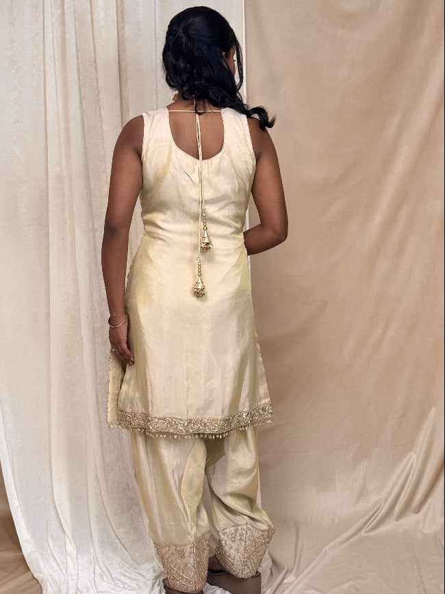 Woman wearing a cream traditional outfit standing in front of beige curtains