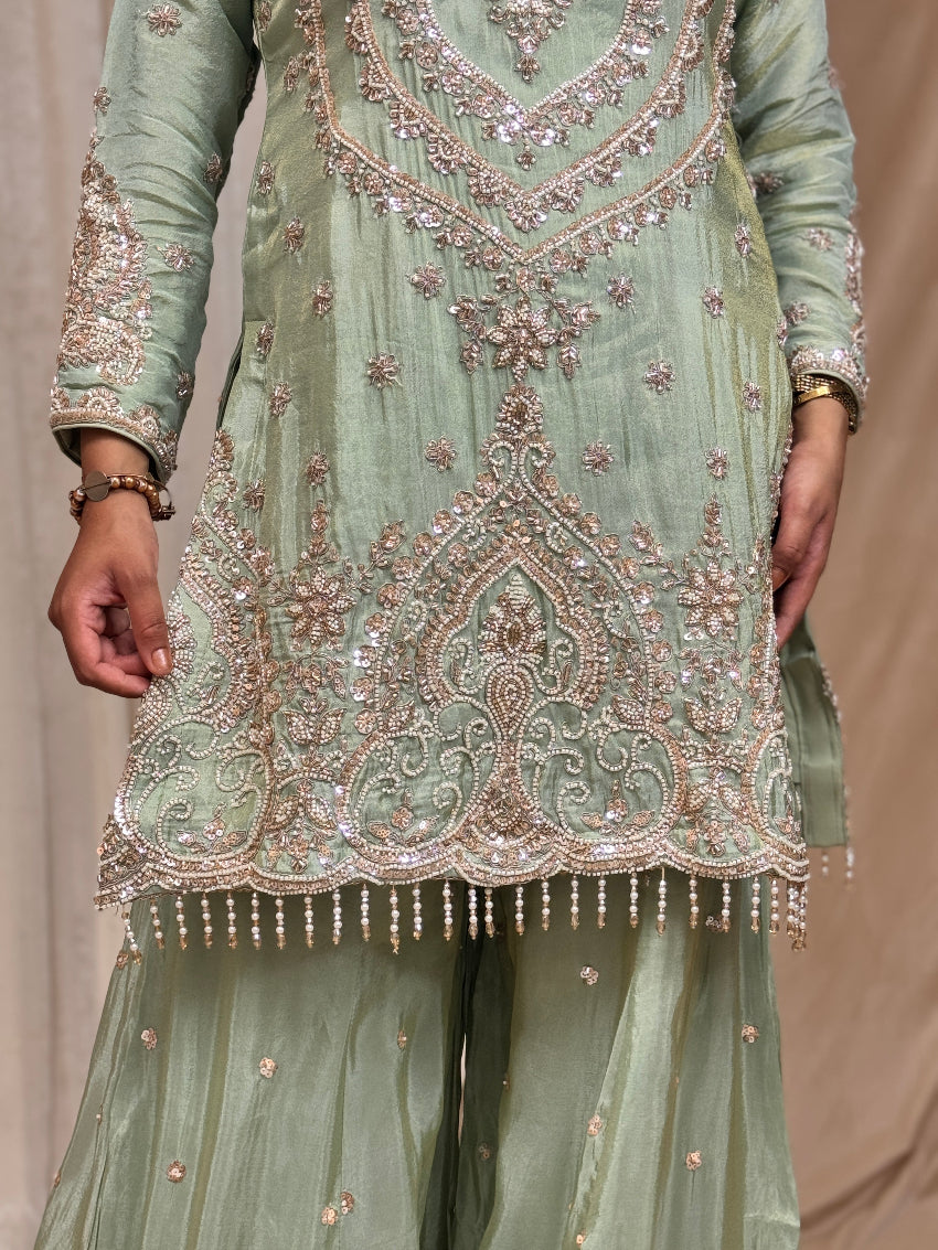 Light green traditional outfit with intricate embroidery on a beige background
