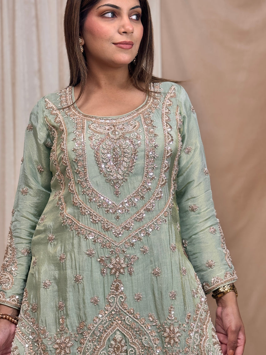 Woman wearing a light green embroidered traditional outfit against a beige background