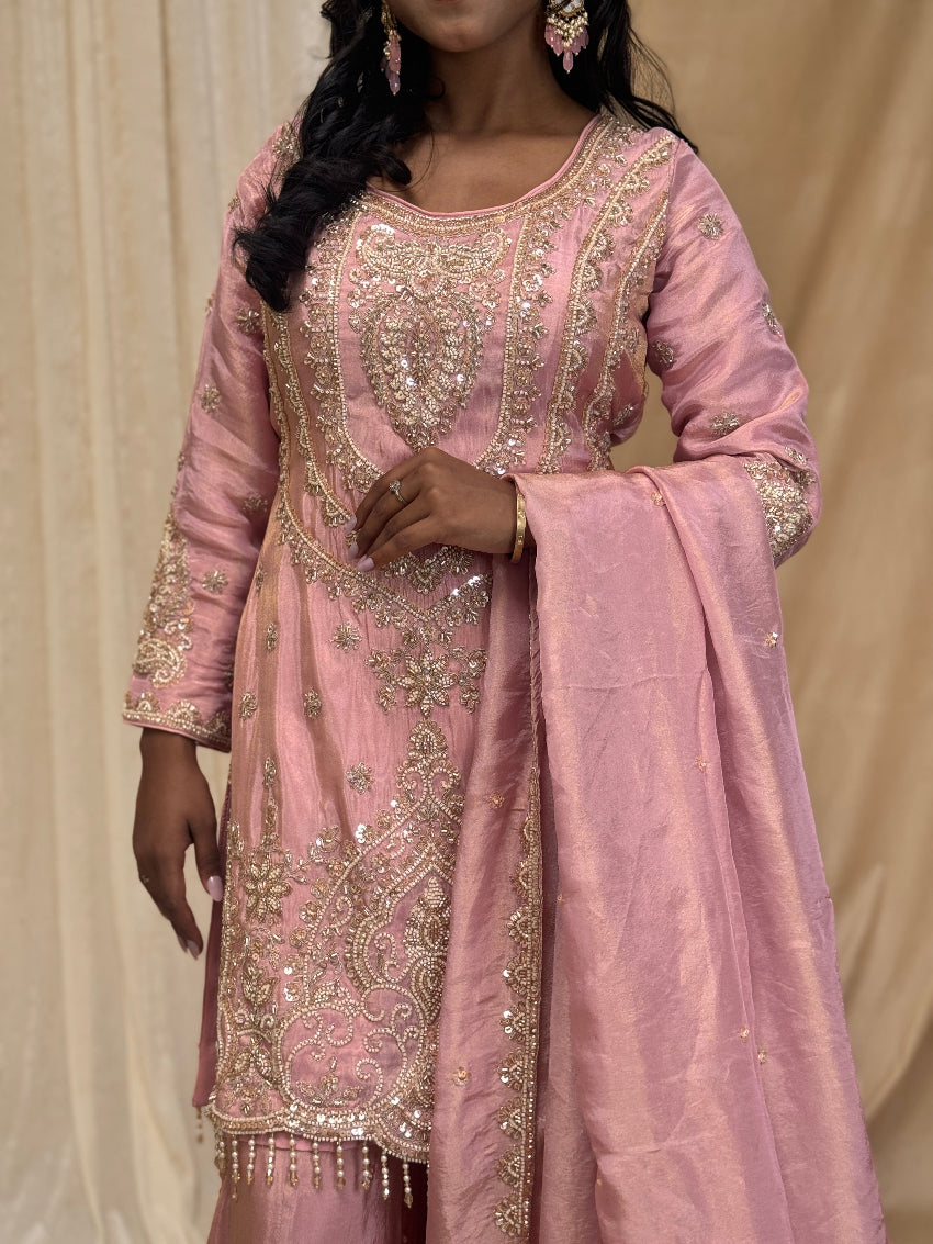 Woman wearing a pink embroidered traditional outfit with a plain background