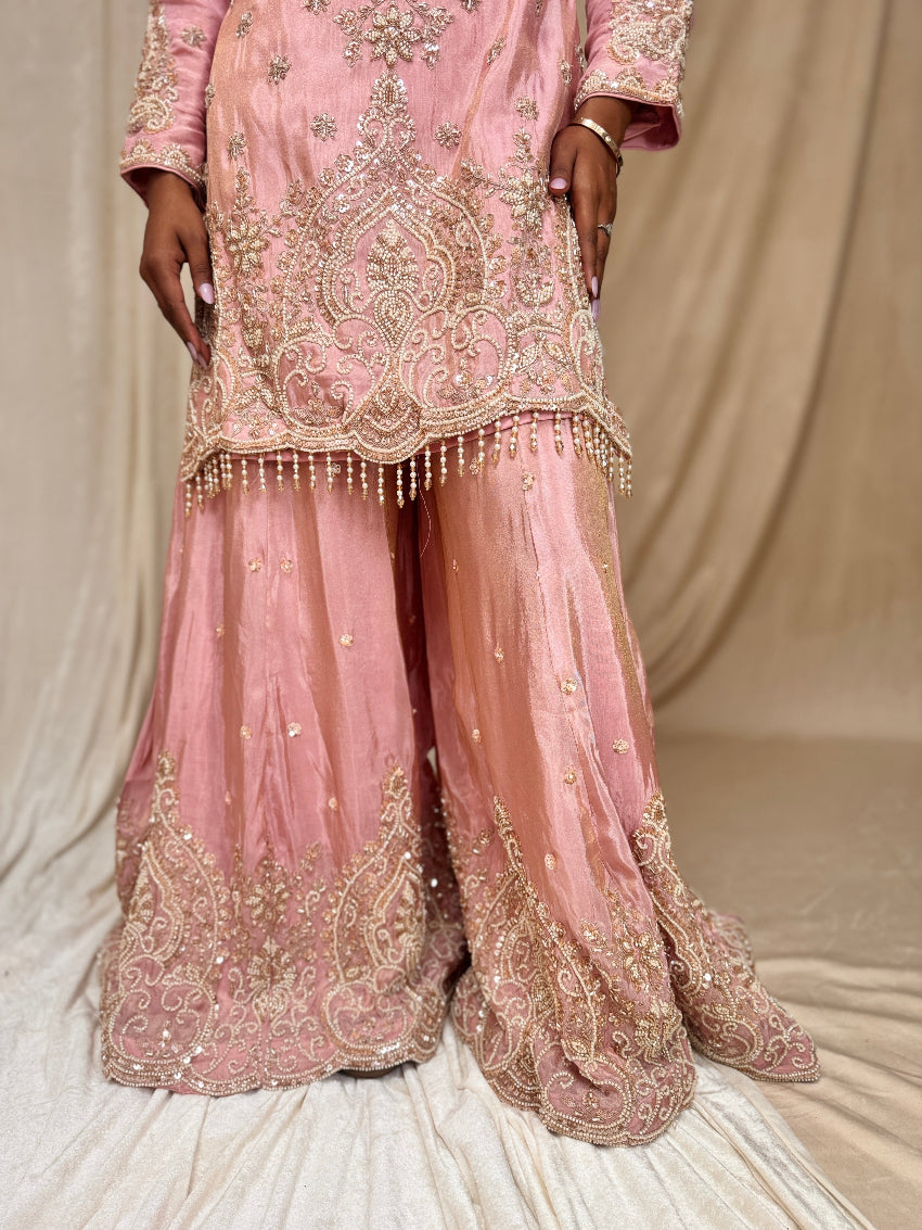 Pink embroidered traditional outfit with gold details on a neutral background