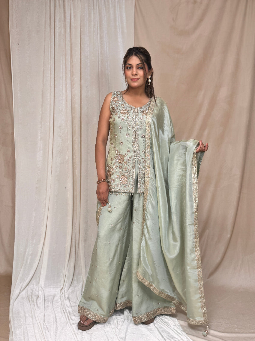 Woman wearing a light green traditional outfit with embroidery against a beige curtain background