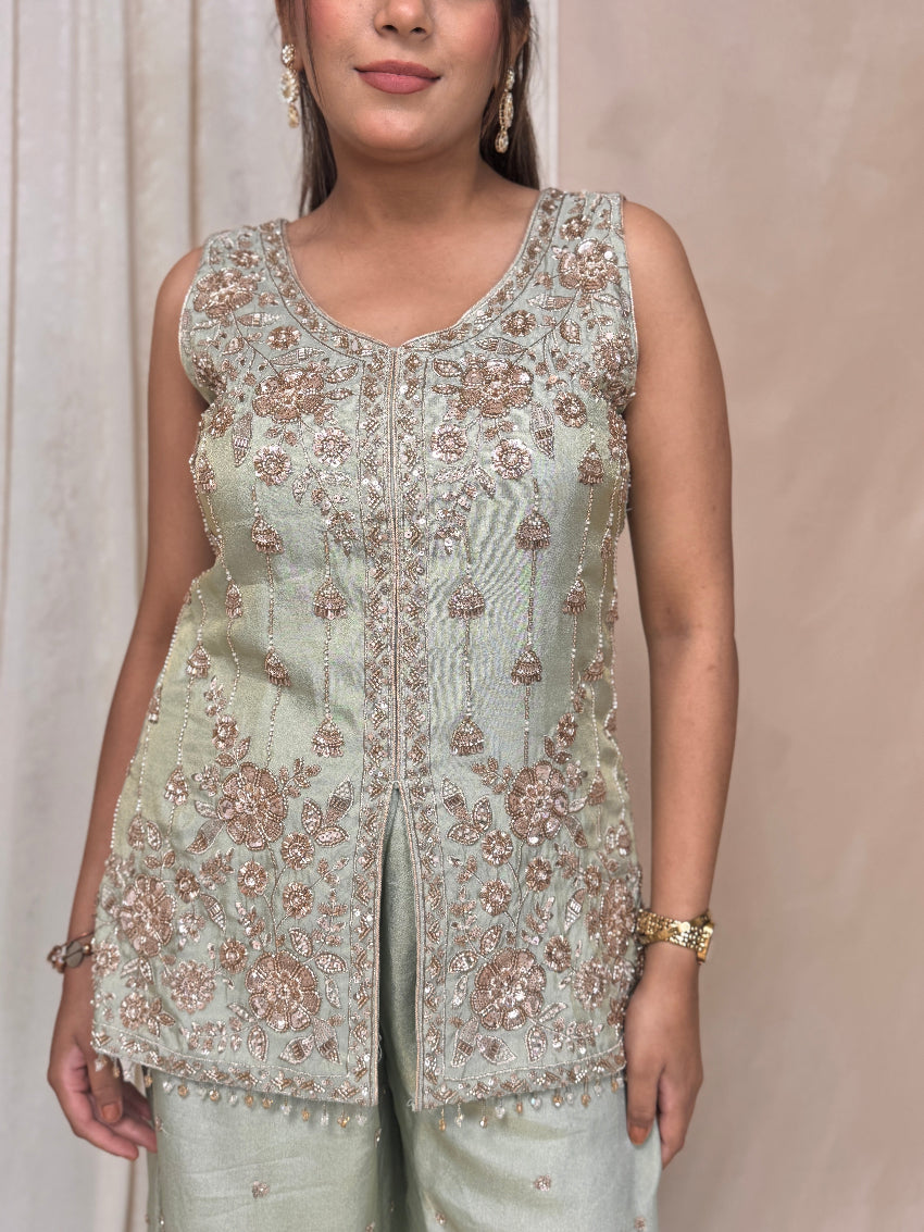Woman wearing a light green embroidered top and pants against a neutral background