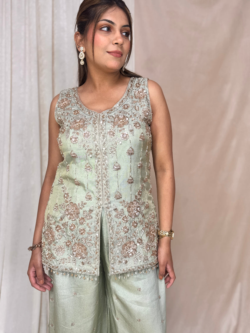 Woman wearing a light green embroidered top and pants against a beige background