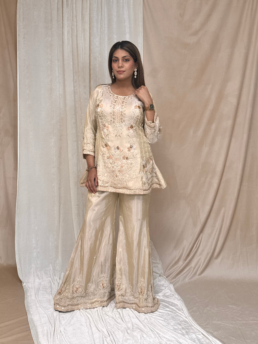 Woman wearing a beige embroidered traditional outfit against a plain background