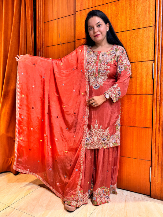 Woman wearing a traditional pink embroidered outfit with a wooden door in the background
