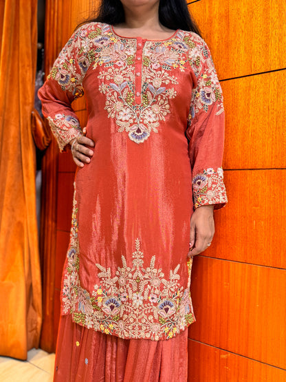 Person wearing a coral pink embroidered traditional outfit against an orange wall.