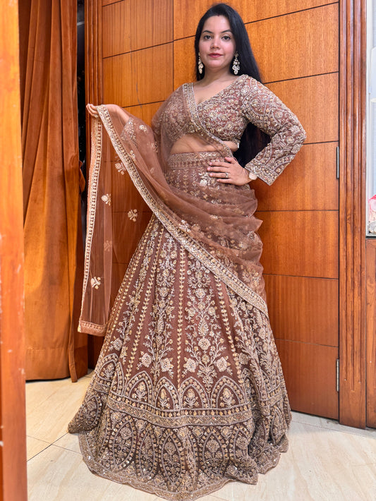 Woman in a traditional brown and beige embroidered outfit standing in front of a wooden door.