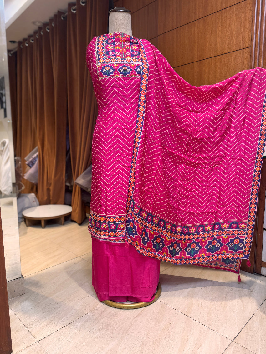Pink traditional outfit with colorful patterns on a mannequin against a wooden panel background.