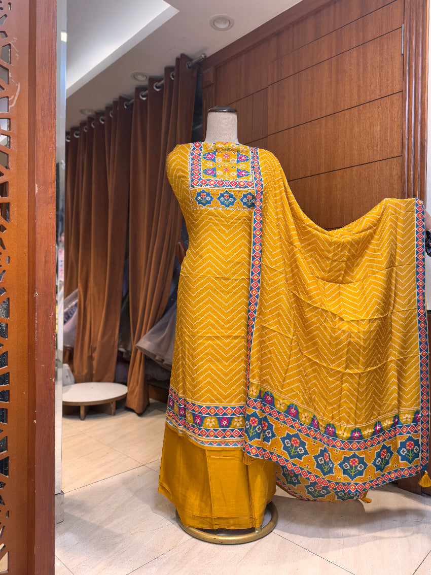 Yellow traditional outfit with colorful patterns on a mannequin against a wooden panel background.