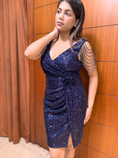 Woman wearing a blue sequin dress against a wooden paneled wall.