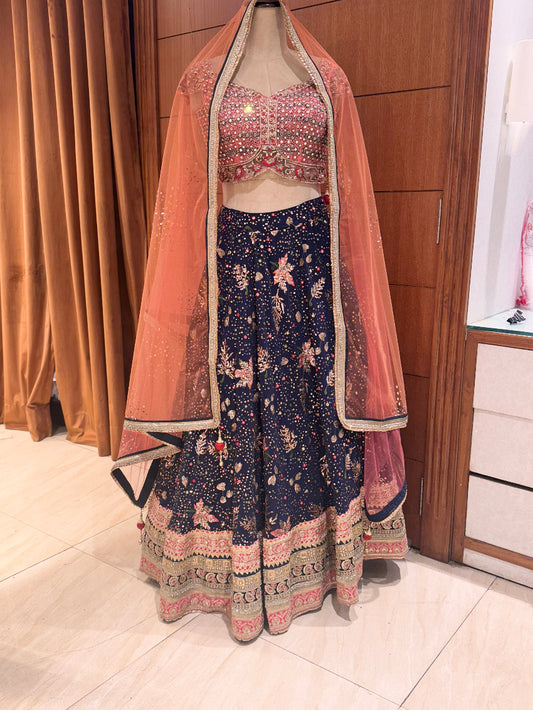 Traditional outfit with a pink dupatta and blue floral pants on a mannequin against a wooden panel background.