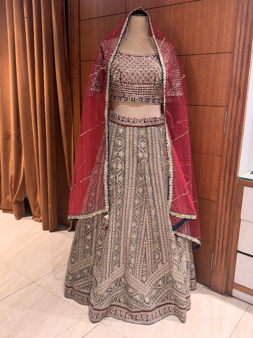 Traditional embroidered outfit with a red dupatta on a mannequin against a wooden panel background.