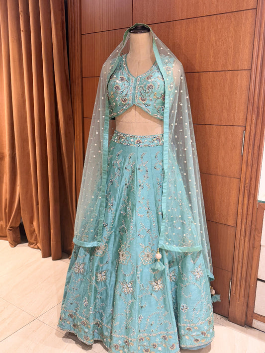 Light blue embroidered lehenga with a dupatta on a mannequin against a wooden panel background