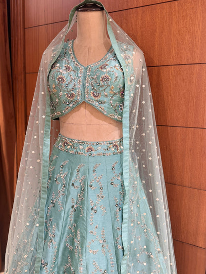 Teal embroidered lehenga with a sheer dupatta on a mannequin against a wooden background