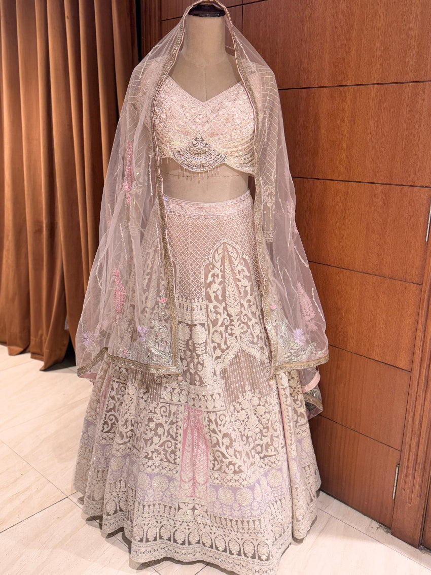 Traditional embroidered lehenga with matching blouse and dupatta on a mannequin against a wooden panel background.