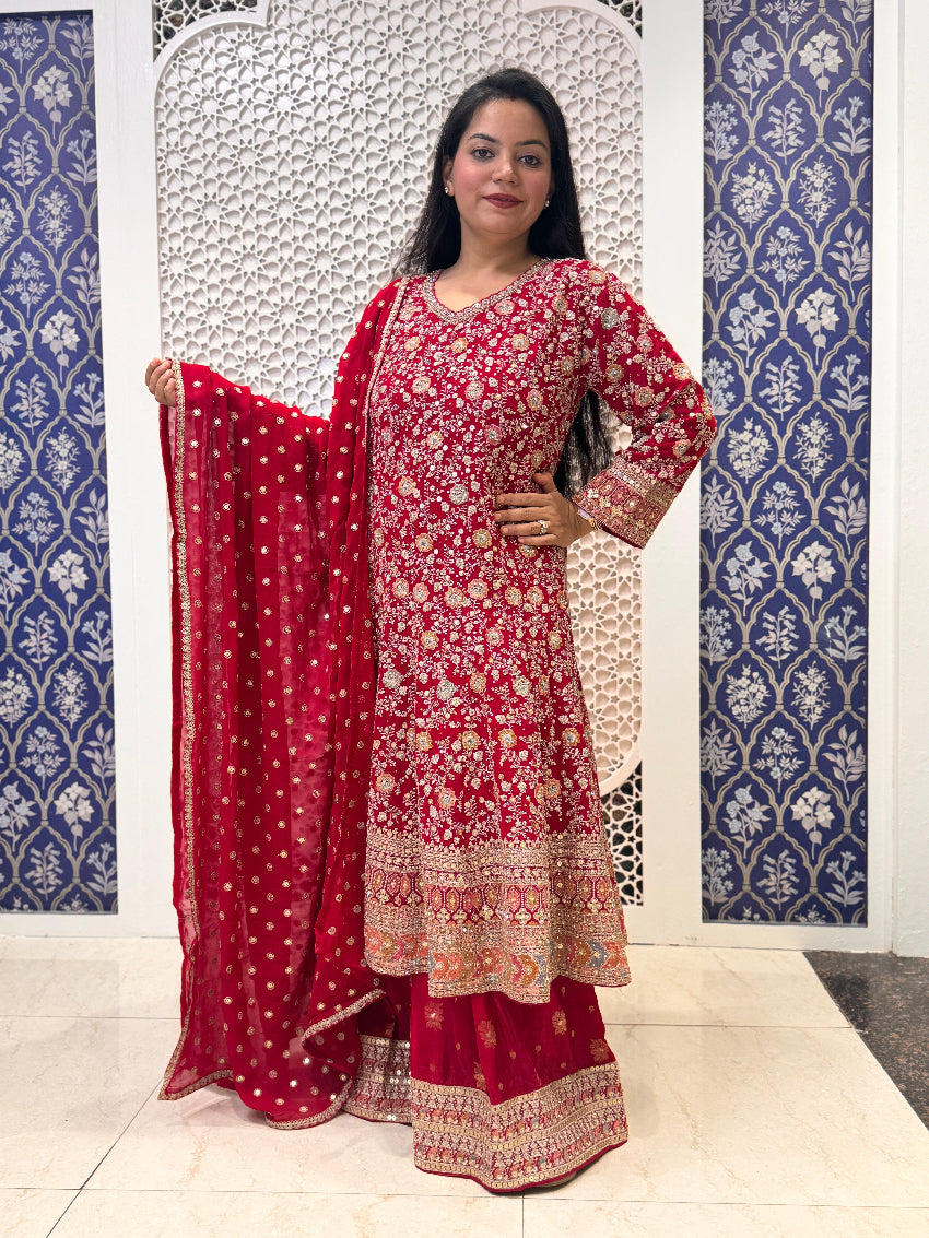 Woman in a red and white traditional outfit standing against a decorative wall.