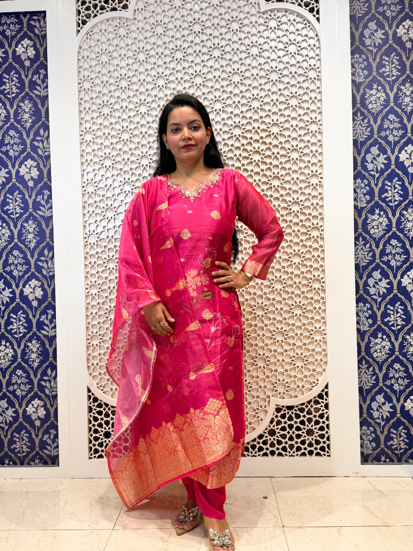 Woman in a pink traditional outfit standing against a decorative wall with blue and white patterns.