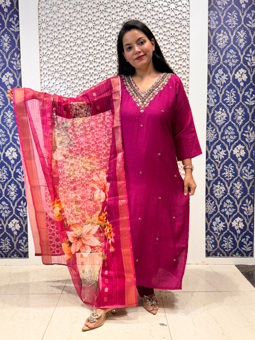 Woman wearing a pink traditional outfit with a floral dupatta against a patterned wall.