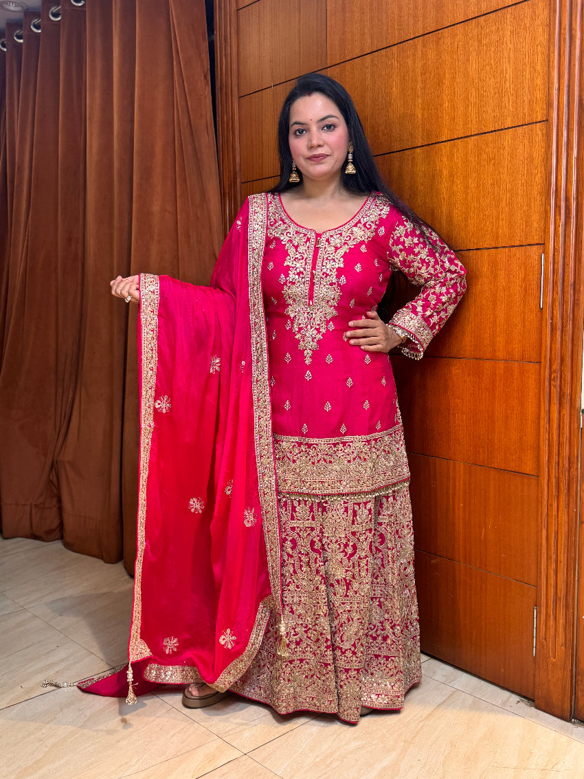 Woman in a traditional pink and gold outfit standing against a wooden door.