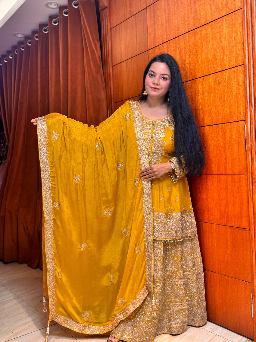 Woman in a yellow and gold traditional outfit standing against a wooden panel background