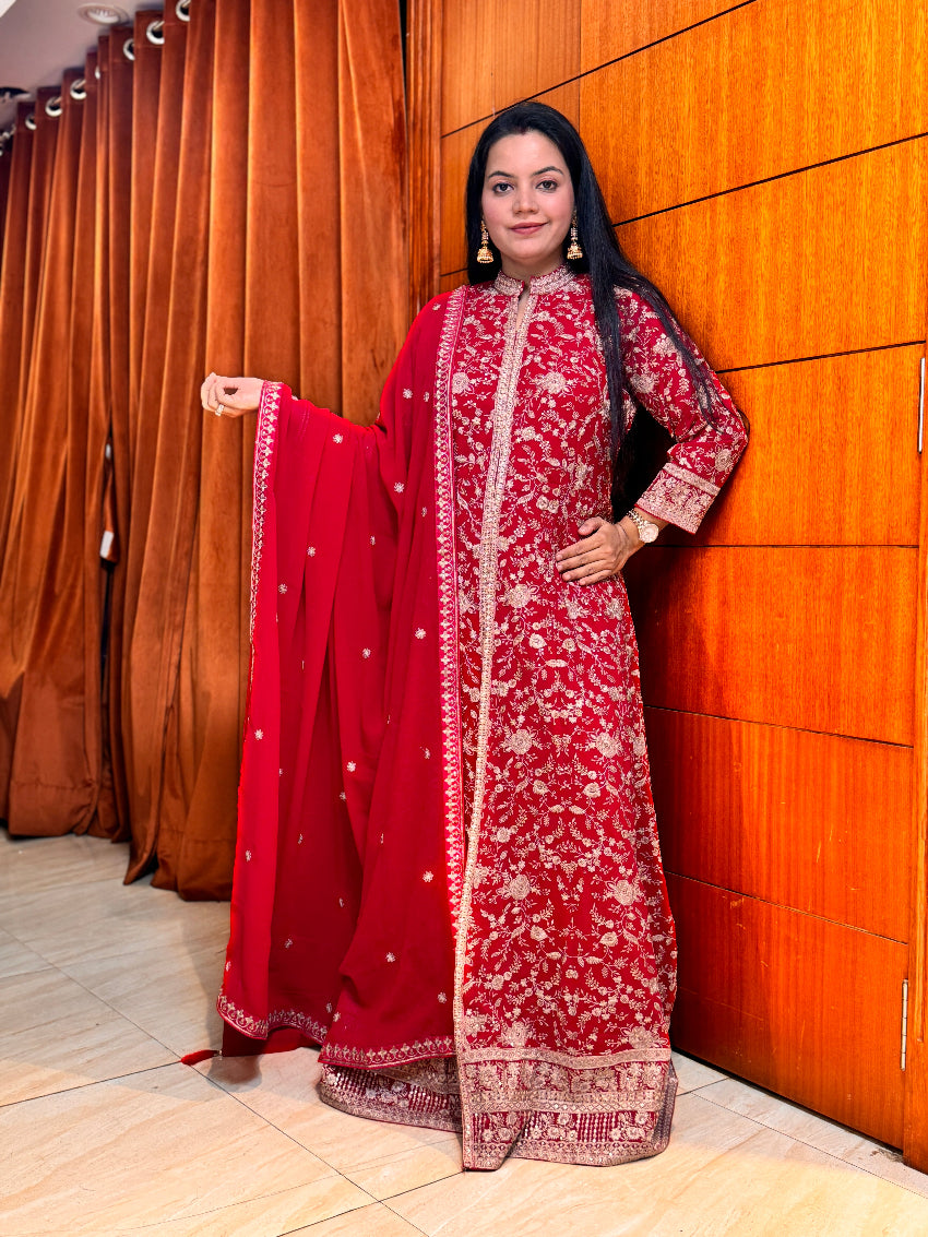 Woman in a red and white traditional outfit standing against an orange wall.