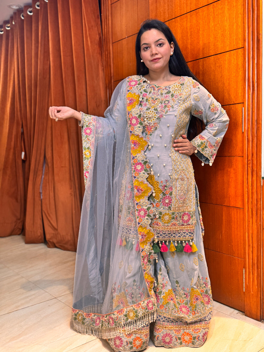 Woman wearing a traditional embroidered outfit with a floral design in front of a wooden panel.