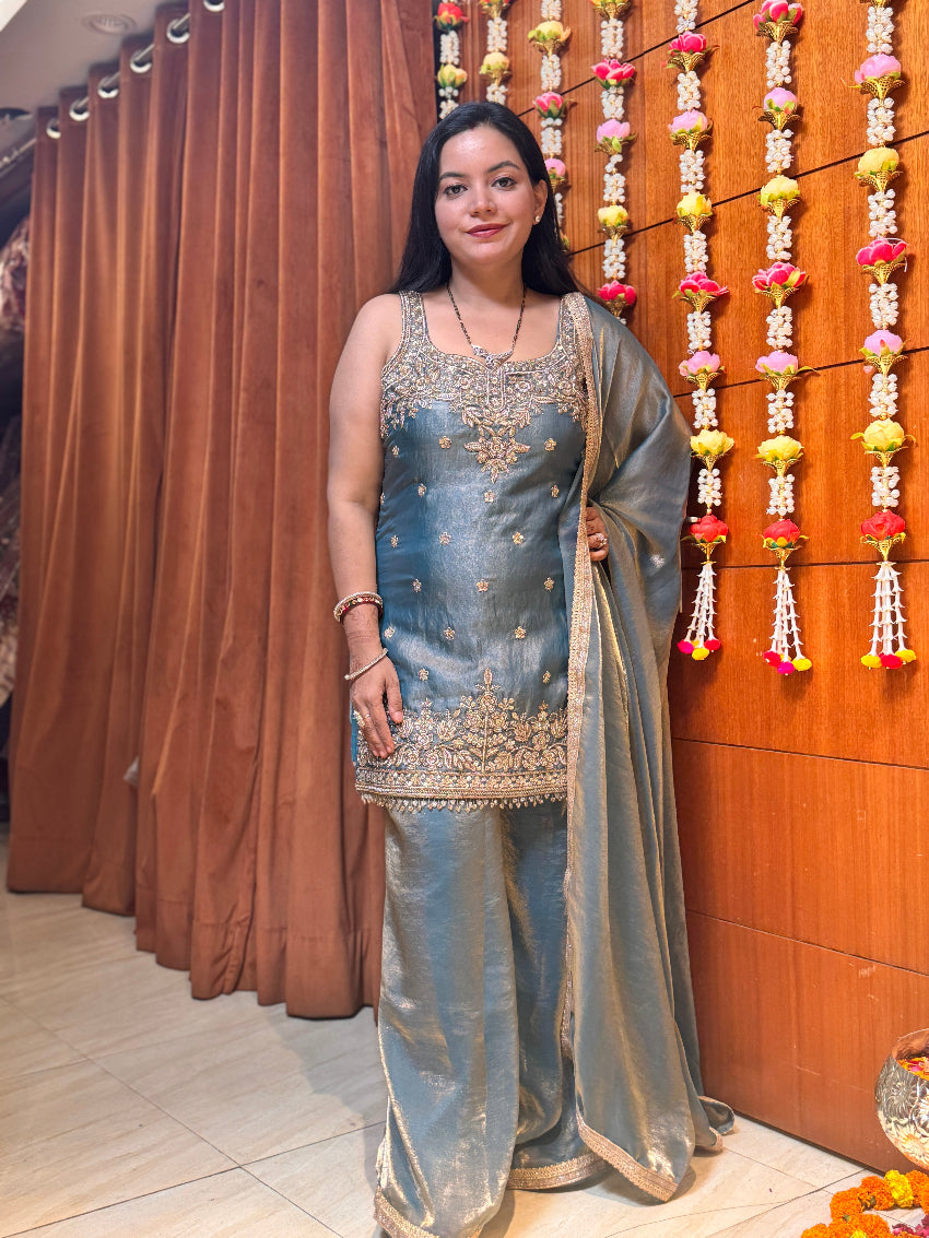 Woman in traditional attire standing in front of a decorative wall with hanging flowers.