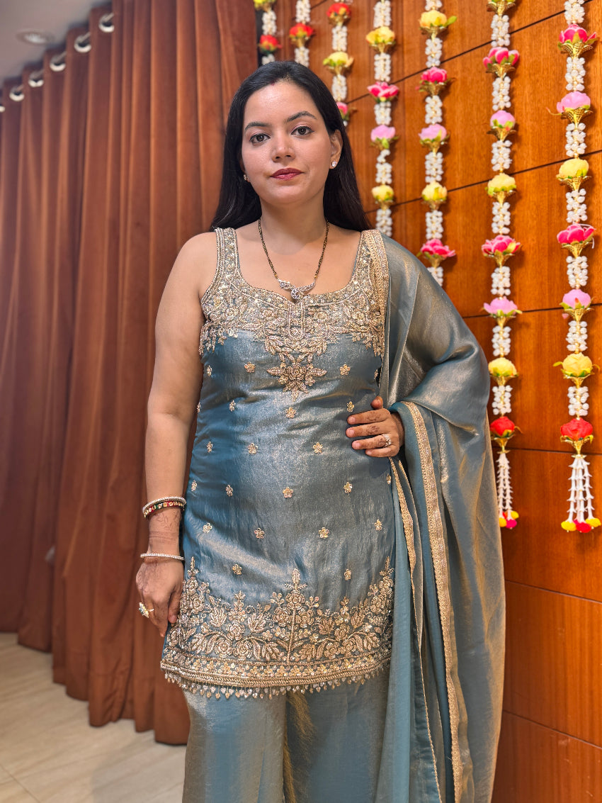 Woman in traditional attire standing in front of a decorative wall with hanging flowers.