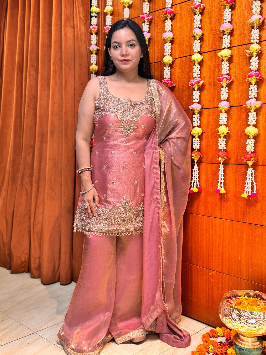Woman in a pink traditional outfit standing in front of a decorated wall with flowers.