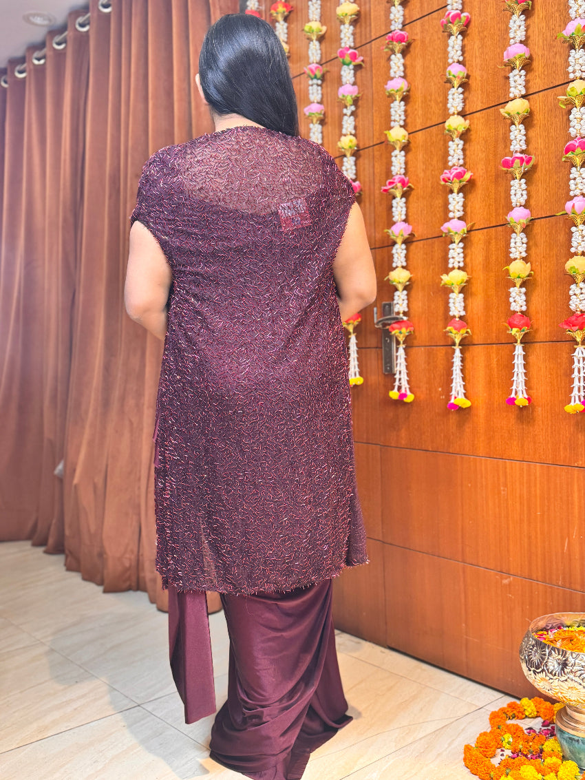 Person wearing a purple traditional outfit in front of a decorated wall.
