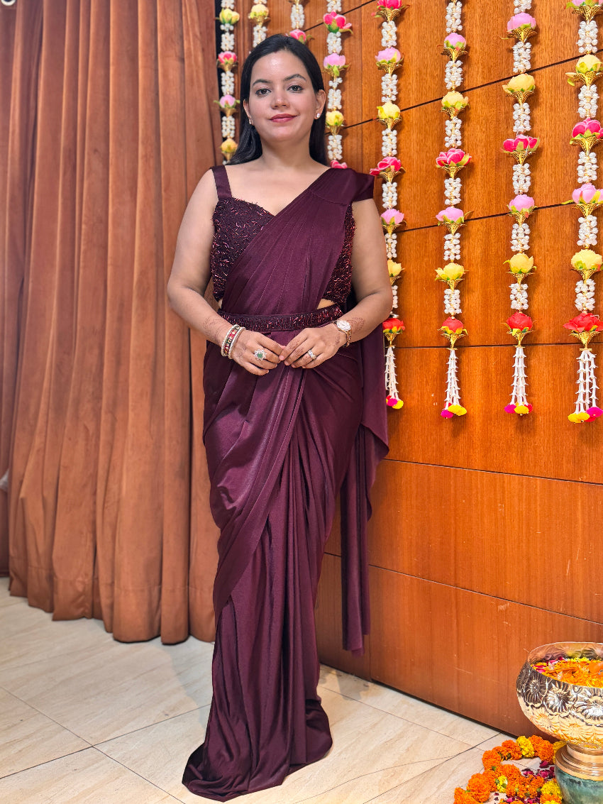 Woman in a purple saree standing in front of a decorated wall with flowers.