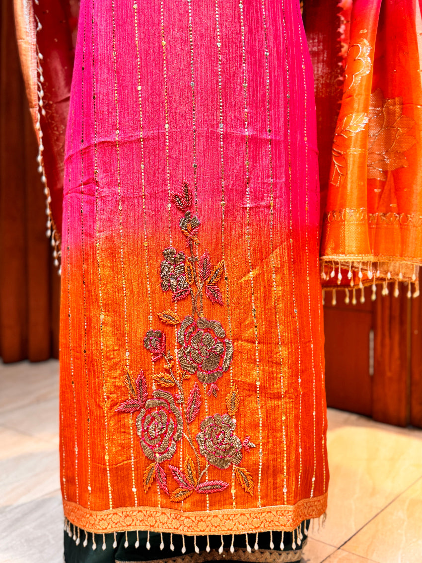 Orange and pink embroidered fabric with floral patterns on a wooden surface.
