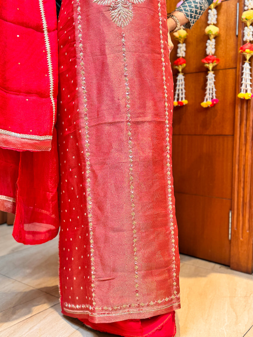 Red saree with intricate patterns held by a person, wooden door in the background