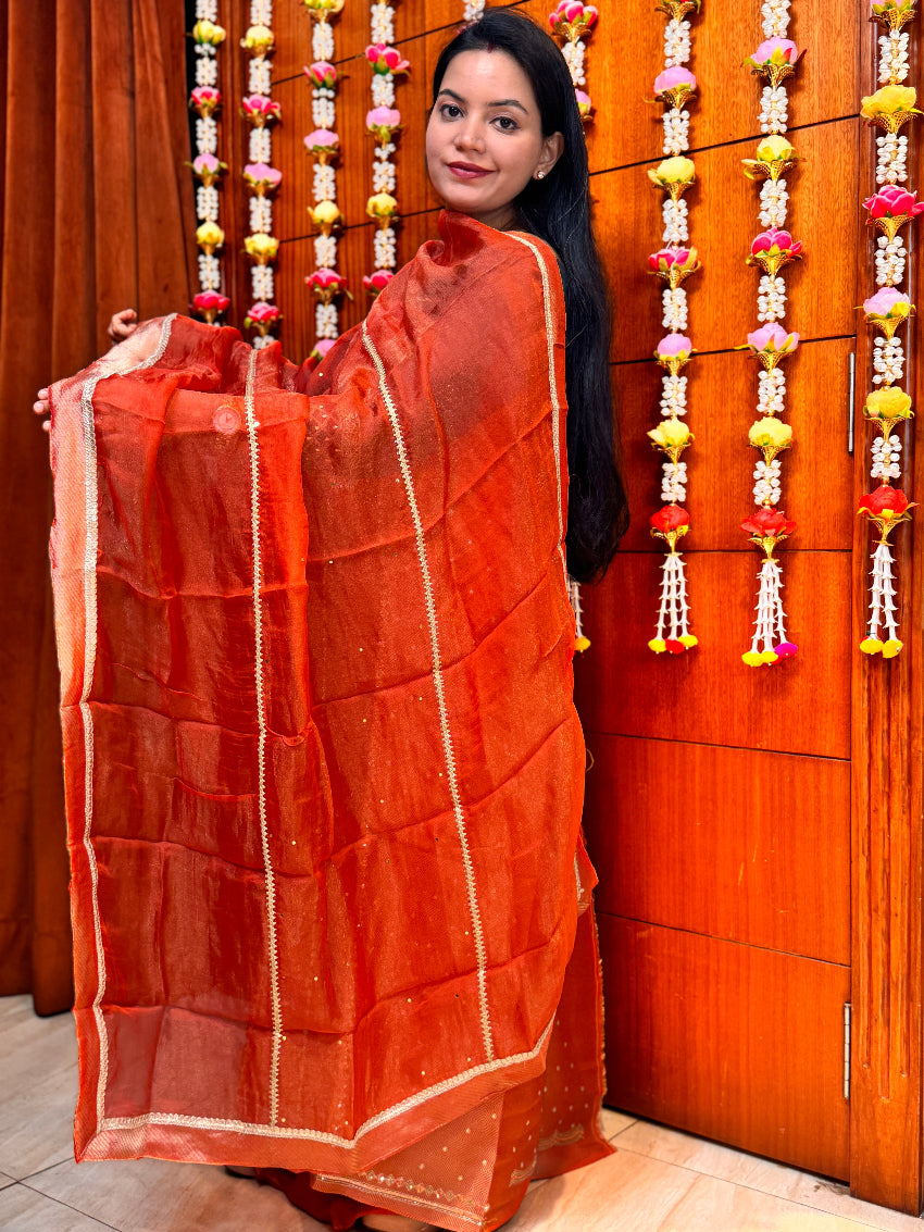 Woman holding an orange saree with a decorative background