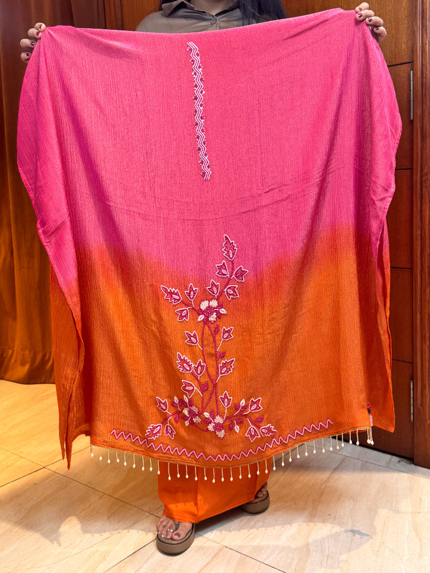 Saree with pink and orange gradient and floral embroidery on a wooden surface.