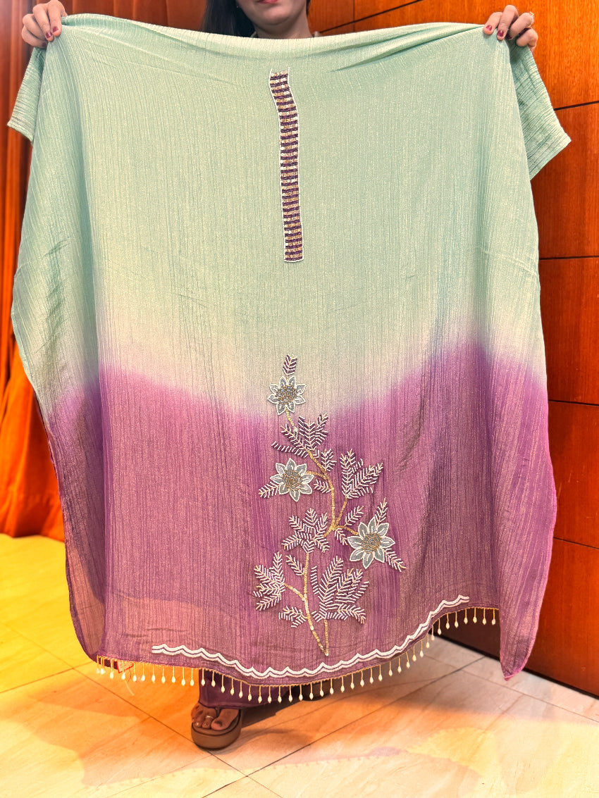 Person holding a light green and purple scarf with floral embroidery.