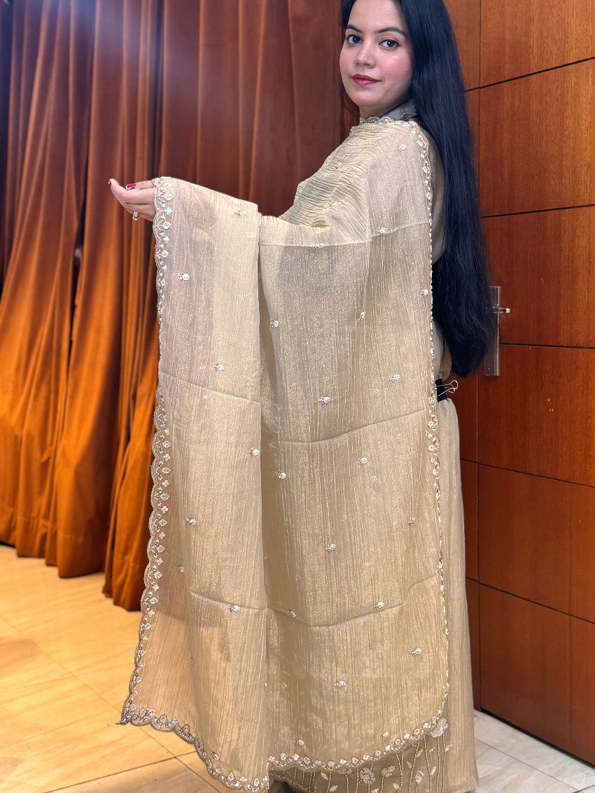 Woman wearing a beige embroidered traditional outfit in front of wooden panels.
