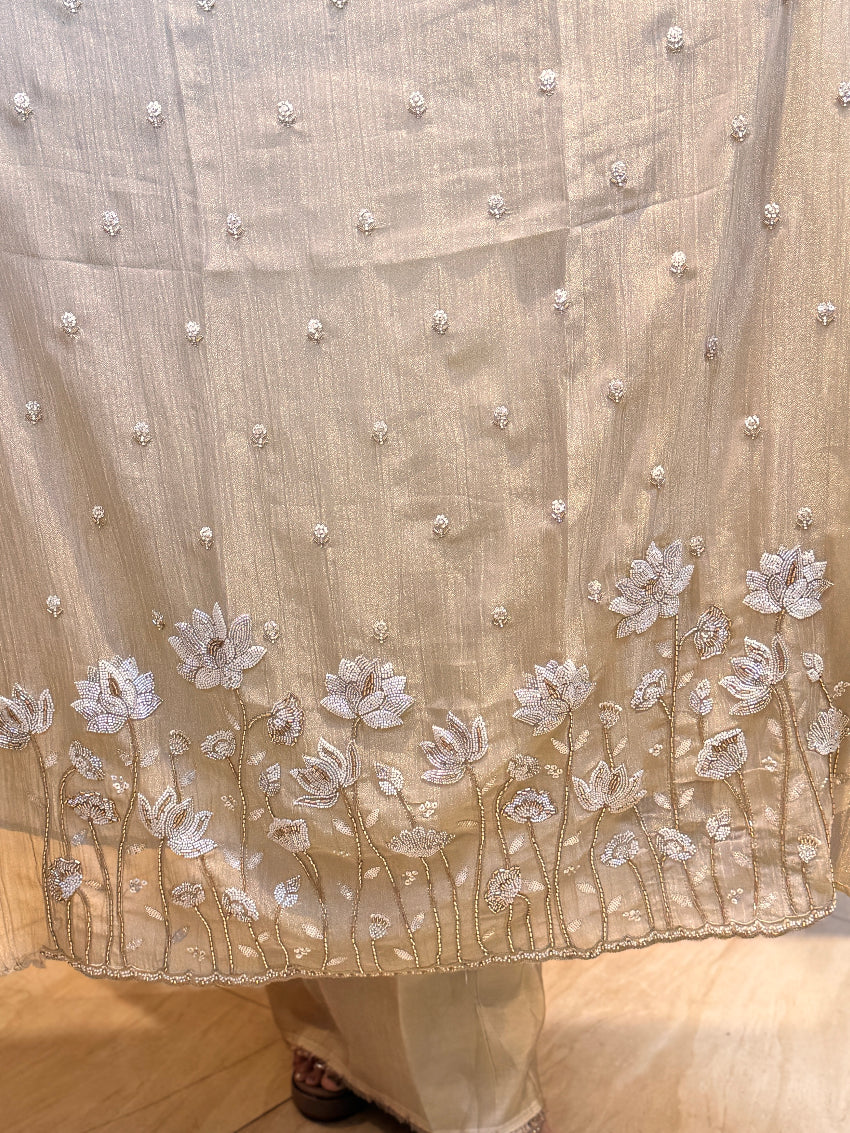 Beige fabric with floral embroidery and pearl embellishments on a wooden floor.