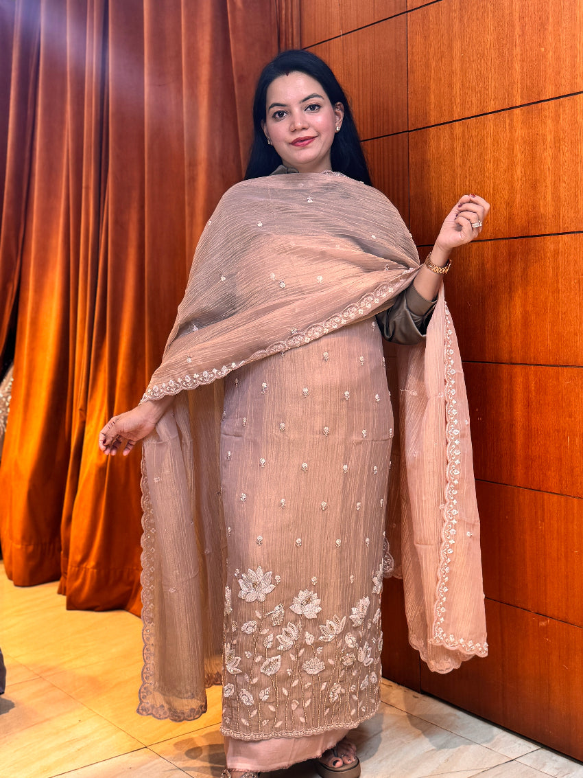 Woman in a beige embroidered traditional outfit standing against a wooden wall.